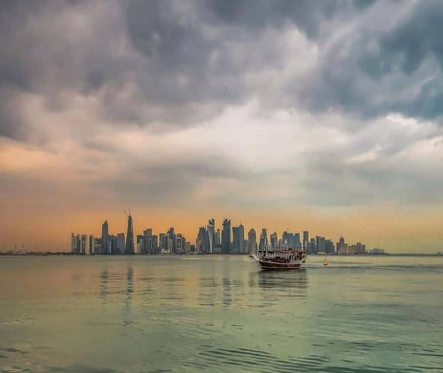 Doha : Harbor Dhow Cruise Tour with Refreshments & Transfers - Boarding a wooden boat with a modern skyline ahead